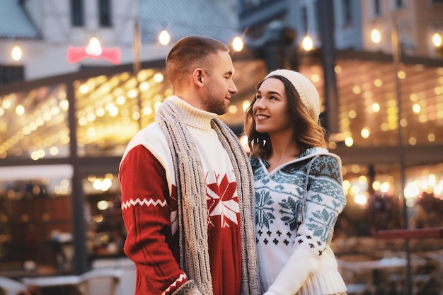 Encantadora pareja se siente feliz en el mercado navideño, rodeada de luces cálidas.