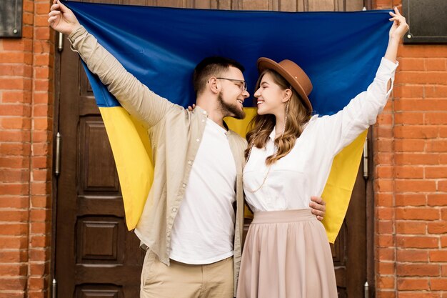 Foto encantadora pareja sonriendo con la bandera de ucrania y la eleva a la cima en honor al amor de la victoria