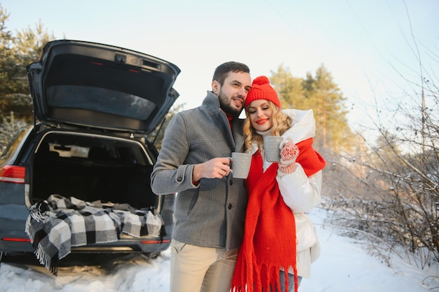 Encantadora pareja sonriente sentada en el maletero del coche en el bosque de invierno