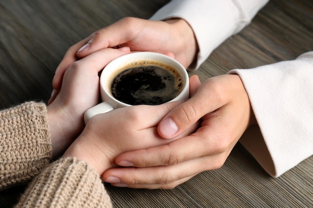 Encantadora pareja sosteniendo una taza de café en las manos sobre fondo de madera