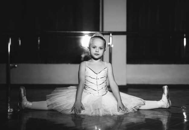 Encantadora pequeña bailarina en tutú blanco haciendo hilo aislado en el fondo del estudio Retrato de bailarina flexible sentada en el suelo en hilo Blanco y negro Primer plano