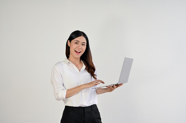 Una encantadora trabajadora de oficina asiática se encuentra sobre un fondo blanco aislado con una laptop