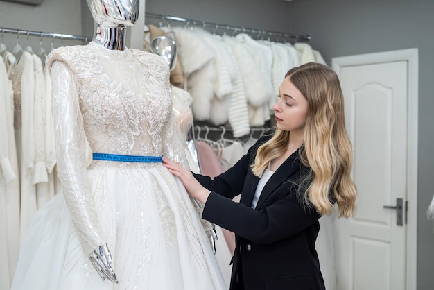 Encantadora vendedora de terno preto elegante mede vestido de noiva com fita métrica na boutique