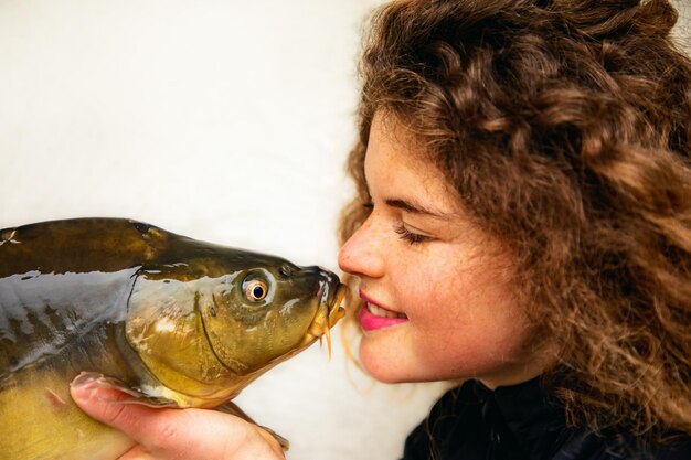 Le encantan los peces. Una mujer joven y hermosa con rizos y una carpa en la mano.