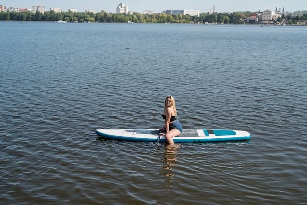 Encante a jovem numa prancha de remo SUP no lago da cidade, feriado no verão