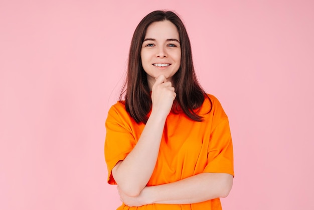 Encanto radiante hermosa mujer con sonrisa encantadora mano en la barbilla posa con gracia en centrico rosa