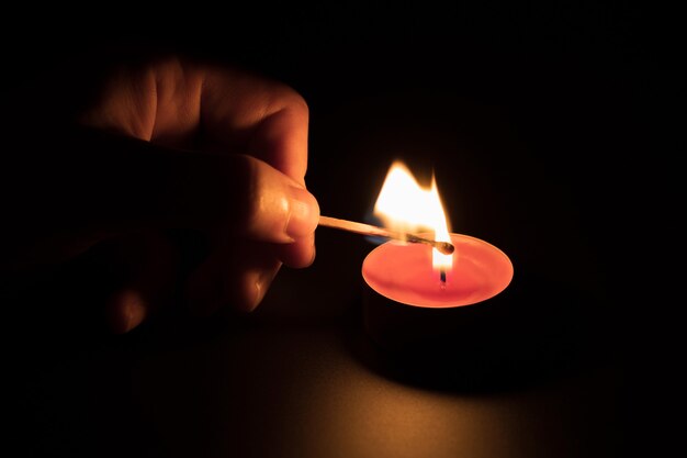 Encender una vela roja con un fósforo en la oscuridad. Concepto de memoria. Fondo negro.