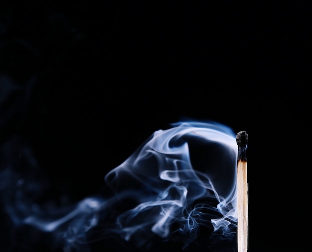 Foto encendido de un fósforo, con humo sobre fondo oscuro. mano sujetando un fósforo ardiente