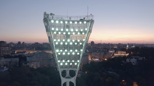 Encendiendo la torre de luz de un estadio de fútbol contra una puesta de sol y una ciudad nocturna cinematográfica