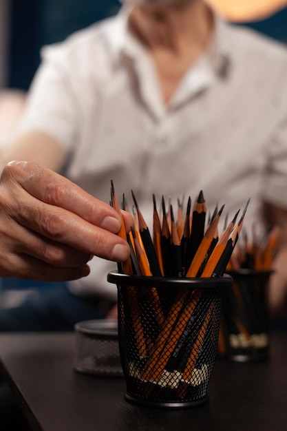 Encerramento da mão do artista aposentado idoso escolhendo um lápis afiado para fazer arte criativa no estúdio doméstico. Pessoa mais velha criativa escolhendo instrumento de desenho profissional para esboço de natureza imóvel.