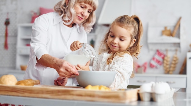 Enche de leite Avó sênior com sua neta cozinha doces para o Natal na cozinha