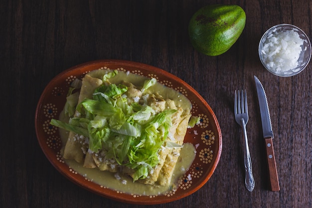 Enchiladas verdes con lechuga servidas en un plato de barro sobre una mesa de madera.