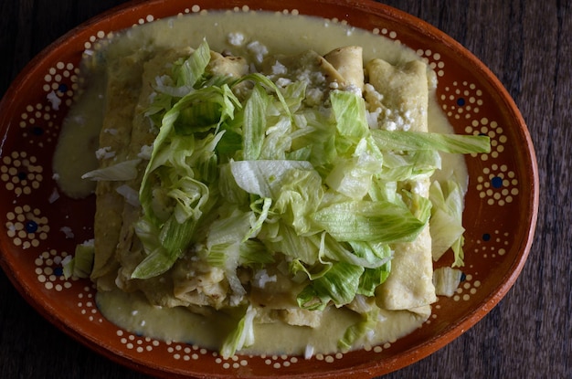 Enchiladas verdes con lechuga servidas en un plato de barro sobre una mesa de madera.