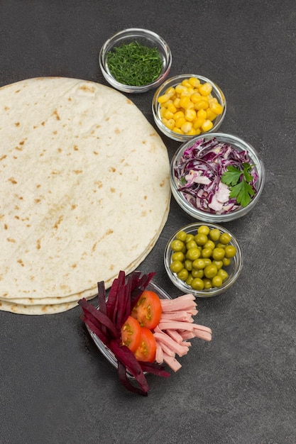 Enchimento de vegetais para tortilha em tigelas de vidro Tortilla envolve fundo preto Flat lay