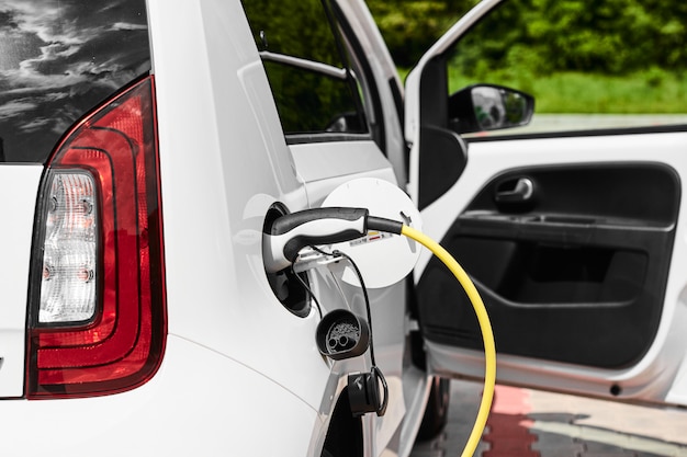 Enchufe eléctrico amarillo que carga un coche eléctrico en la calle. Fuente de alimentación conectada al automóvil eléctrico