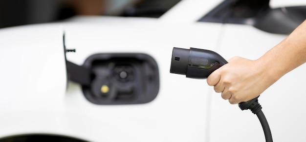 Enchufe EV de sujeción manual con imagen borrosa del coche progresivo en la estación de carga