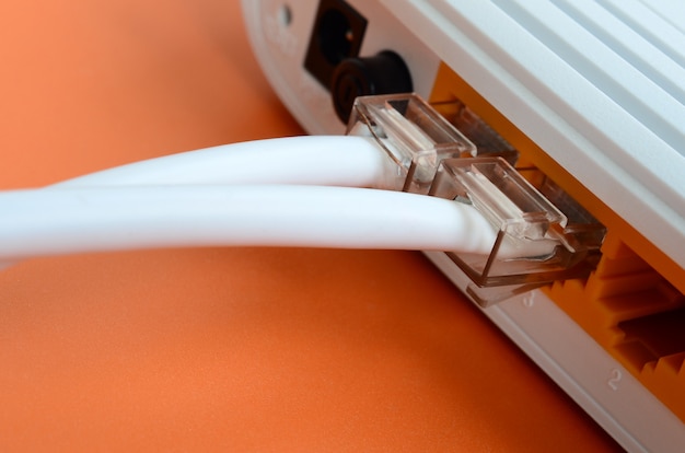Los enchufes del cable de Internet están conectados al enrutador de Internet, que se encuentra sobre un fondo naranja brillante. Artículos requeridos para la conexión a internet