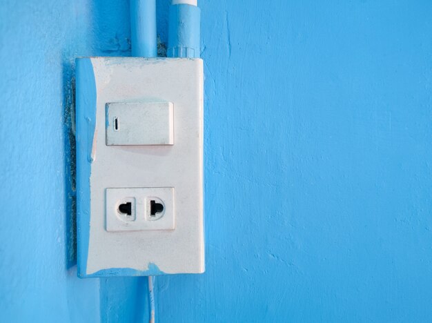 Los enchufes e interruptores antiguos están montados en paredes de cemento azul dentro del edificio.