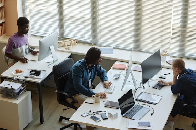 Por encima del ángulo de varios ingenieros de TI interculturales sentados frente a las computadoras