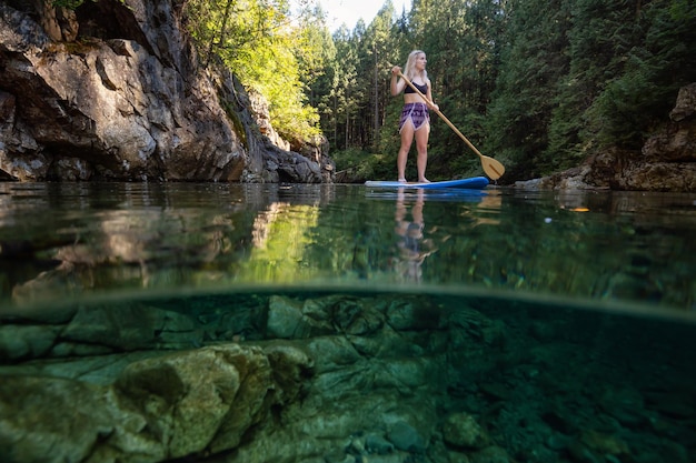 Por encima y por debajo de la imagen de una joven caucásica haciendo paddle surf en un río