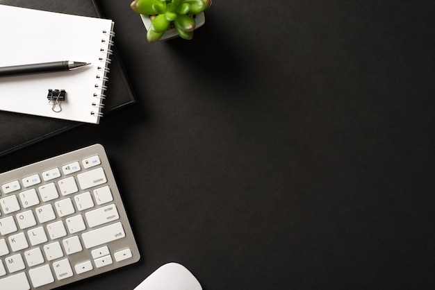 Encima de la foto de vista superior del lugar de trabajo elegante con teclado inalámbrico suculento clip de cuaderno sobre fondo negro con espacio vacío en blanco