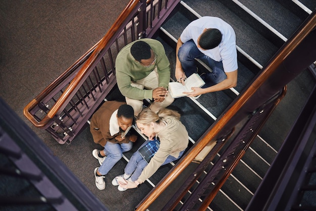 Por encima del grupo de estudiantes y las escaleras para leer juntos, estudiar e investigar para el examen o la educación Diversidad de estudiantes y trabajo en equipo para objetivos de éxito y motivación en el campus universitario o enfoque