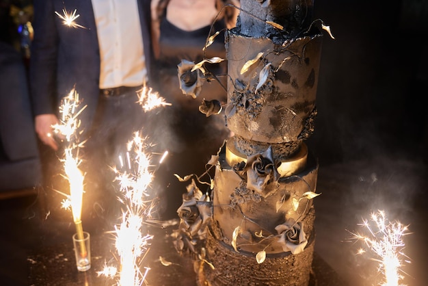 Por encima de las velas encendidas, los fuegos artificiales se colocan en un pastel y una mano se cierne sobre él