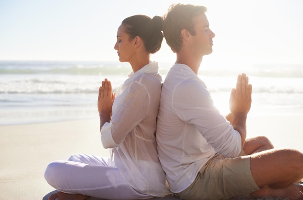 Encontrando tranquilidade um com o outro Um jovem casal realizando uma relaxante rotina de ioga juntos na praia