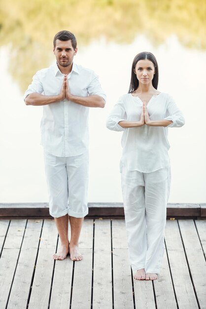 Encontrar paz juntos. comprimento total de um lindo casal jovem em roupas brancas meditando ao ar livre juntos