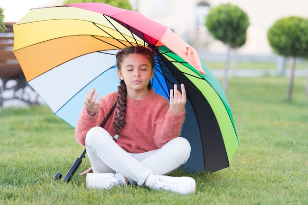 Encontre um espaço privado tranquilo para relaxar. Sob um grande guarda-chuva. Cabelo comprido de criança menina meditar no parque sob o guarda-chuva. Fique positivo e otimista. Influência positiva de acessórios coloridos. Guarda-chuva brilhante.