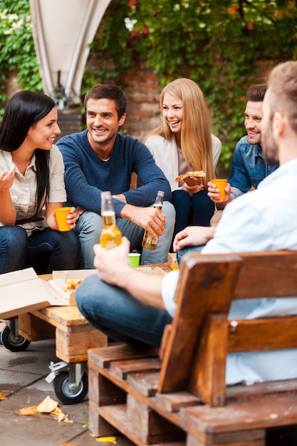 Encontro com os melhores amigos. grupo de jovens alegres conversando e comendo pizza sentados ao ar livre