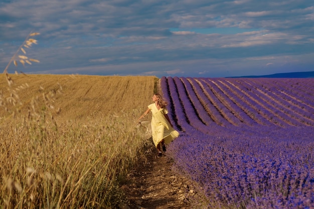 Encontro de dois mundos: uma garota em um vestido amarelo entre um campo de trigo e lavanda