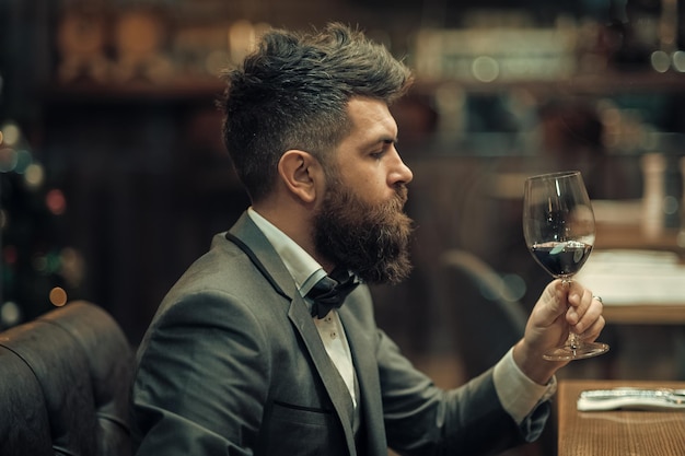 Encontro de encontro de hipster esperando no pub. Vinho perfeito. cliente bar sente-se no café bebendo álcool. Empresário com bebida de barba longa no clube de charutos. Homem barbudo descansar no restaurante com copo de vinho.