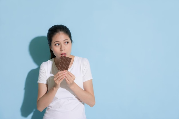 Se encontró una joven hermosa que tenía un problema de caries dental sobre fondo azul y robaba comer chocolate mirando el área vacía.