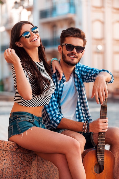 Encontro perfeito. Jovem casal apaixonado se unindo e olhando para a câmera enquanto está sentado ao ar livre