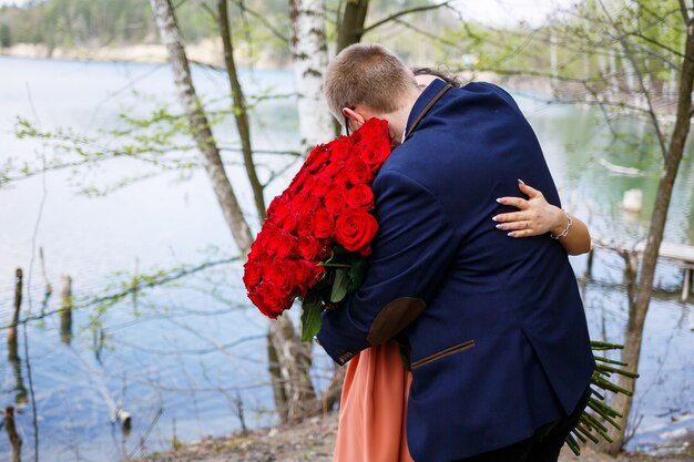 Encontro romântico de jovens. uma jovem concordou em se casar com seu marido. um cara de terno com um buquê de rosas vermelhas dá um buquê para a garota, e eles se beijam na floresta