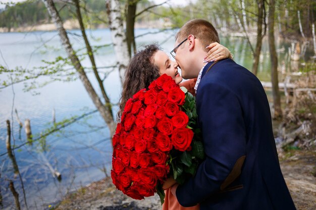 Encontro romântico de jovens. uma jovem concordou em se casar com seu marido. um cara de terno com um buquê de rosas vermelhas dá um buquê para a garota, e eles se beijam na floresta