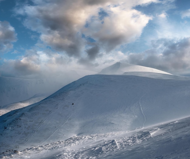 Encosta de montanha coberta de neve na luz do sol da noite passada Magnífico crepúsculo ventoso no topo acima da pitoresca estância de esqui alpina Dragobrat Ucrânia Carpathian Mountains