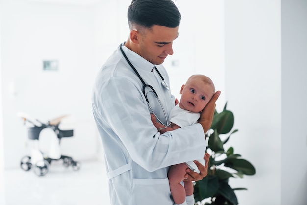 Foto encosta na janela. jovem pediatra está com o bebê na clínica durante o dia.