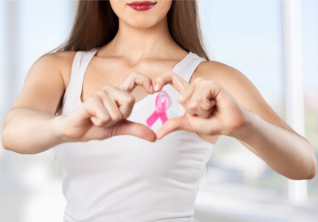 Encuadre del corazón de los dedos en el pecho de la mujer con insignia rosa para apoyar la causa del cáncer de mama,