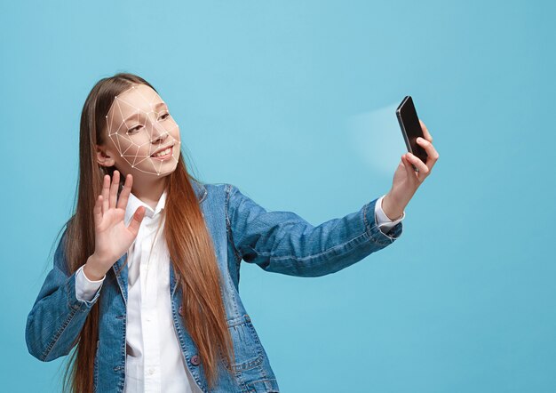 Encuentro de conocimientos. Una chica con un teléfono inteligente en traje de jeans de pie sobre fondo azul. Tecnología de reconocimiento facial en cuadrícula poligonal. Concepto de seguridad cibernética, negocios, trabajo, educación.