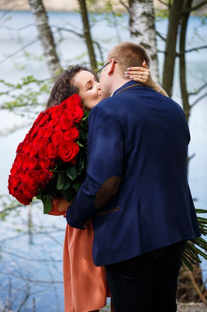 Encuentro romántico de jóvenes. Un chico de traje con un ramo de rosas rojas le da un ramo a la niña y se besan en el bosque.