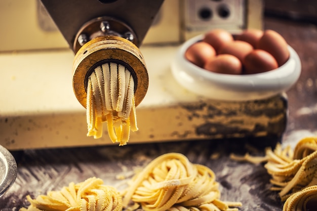 Ende des Nudelherstellungsprozesses mit frischer Fettuccine, die die Nudelmaschine verlässt.