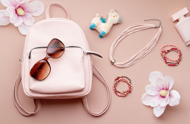 Endecha plana con accesorios de mujer rosa con mochila y mano de mujer sosteniendo las gafas de sol. Tendencias de moda de verano, concepto de compras
