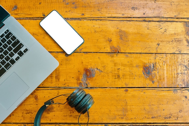 Endecha plana de auriculares portátiles y teléfonos inteligentes en la pantalla de teléfono móvil en blanco de mesa de madera para insertar som ...