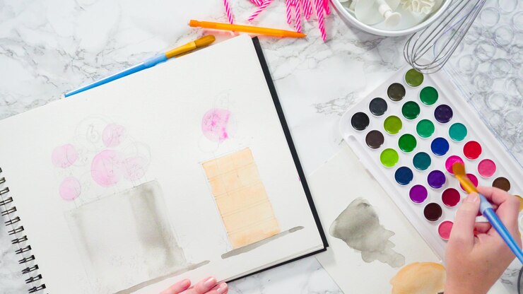 Foto endecha plana. baker está dibujando el diseño de un pastel de cumpleaños con acuarelas.