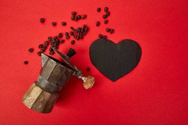 Endecha plana de cafetera y granos de café sobre fondo rojo.