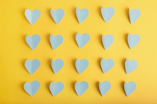 Endecha plana de corazones de papel azul en filas en amarillo