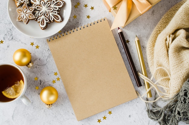 Endecha plana de cuaderno marrón en blanco con caja de regalo, té, galletas y cuadros.