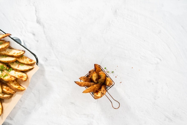 Endecha plana. Cuñas de patatas recién horneadas con especias en una cesta de alambre.